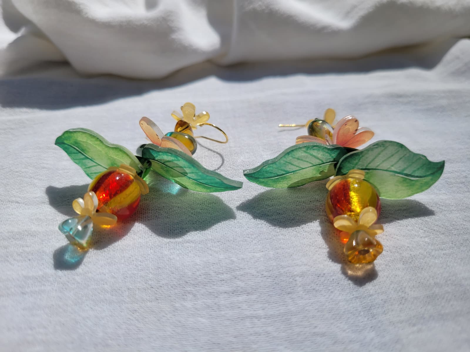 Pair of colorful glass earrings with leaf designs, glass czech beads and butterflies on a light gray background