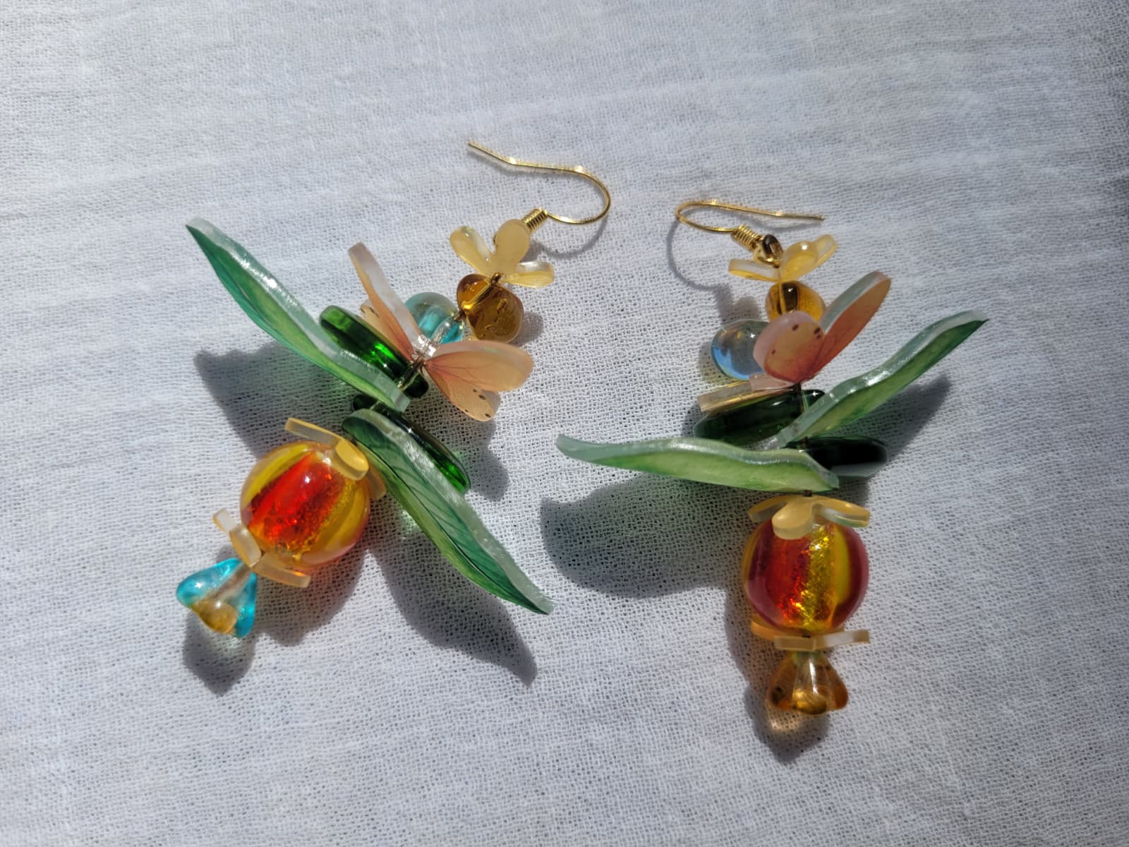 Pair of colorful glass earrings with leaf designs, glass czech beads and butterflies on a light gray background