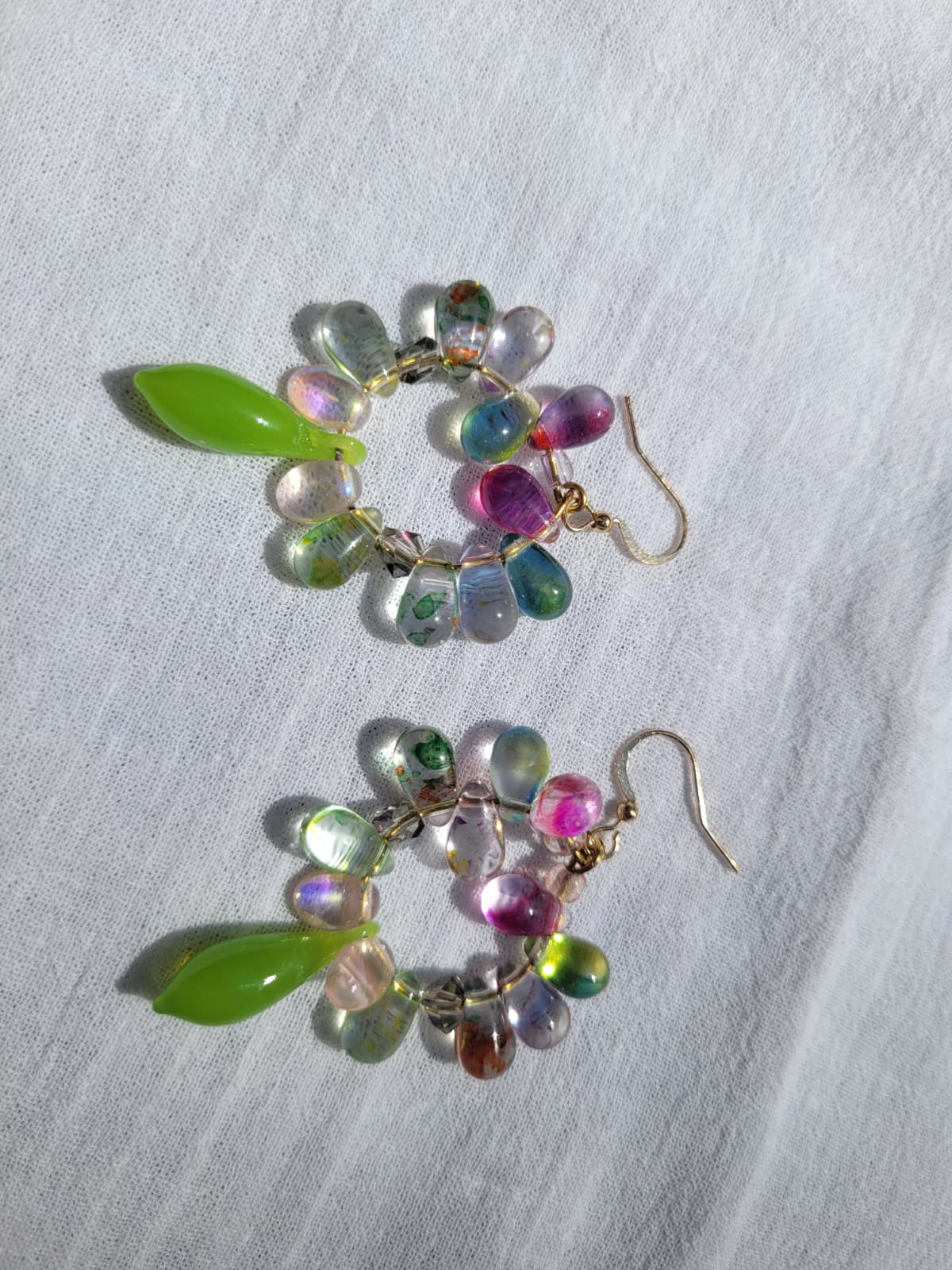 Multicolored round beaded earrings with green and pink accents on a light gray fabric background
