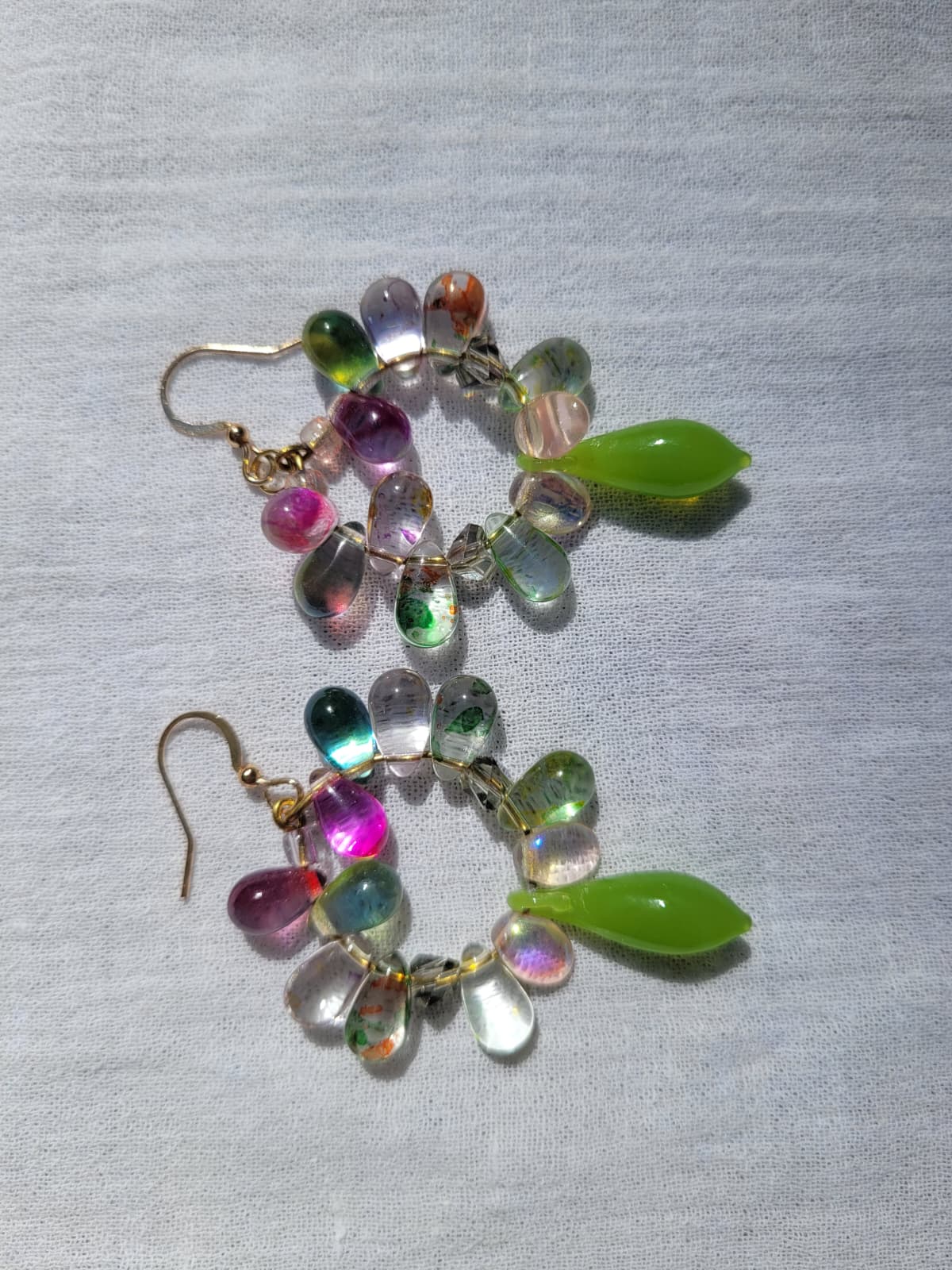 Multicolored round beaded earrings with green and pink accents on a light gray fabric background