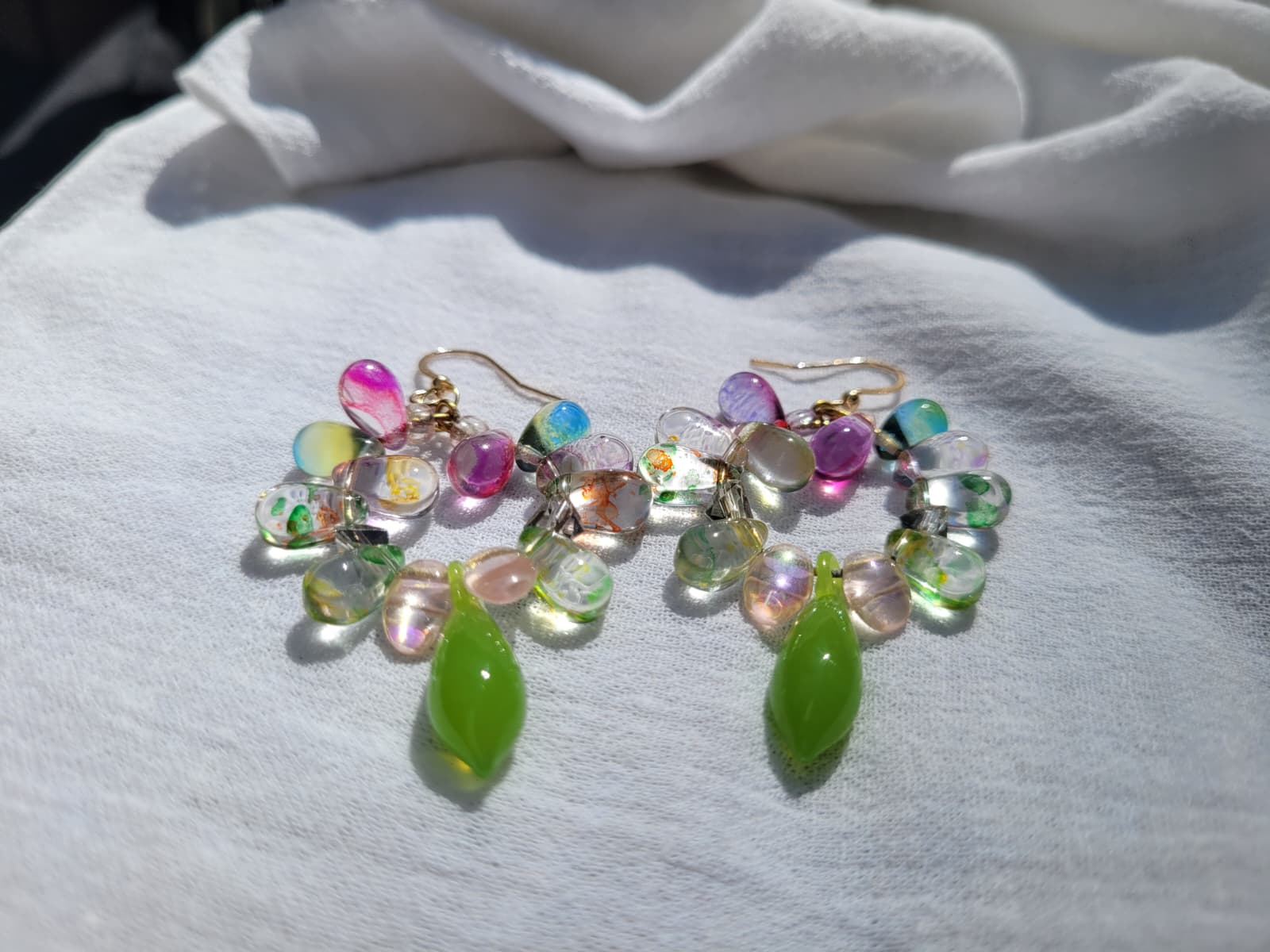 Multicolored round beaded earrings with green and pink accents on a light gray fabric background