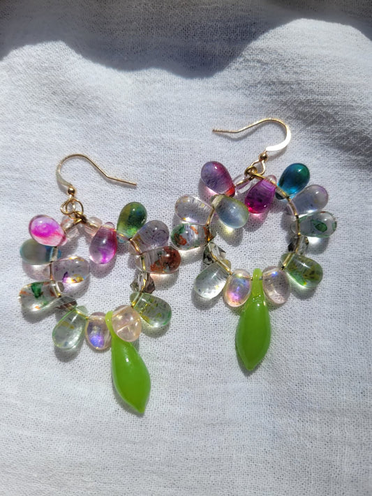 Multicolored round beaded earrings with green and pink accents on a light gray background