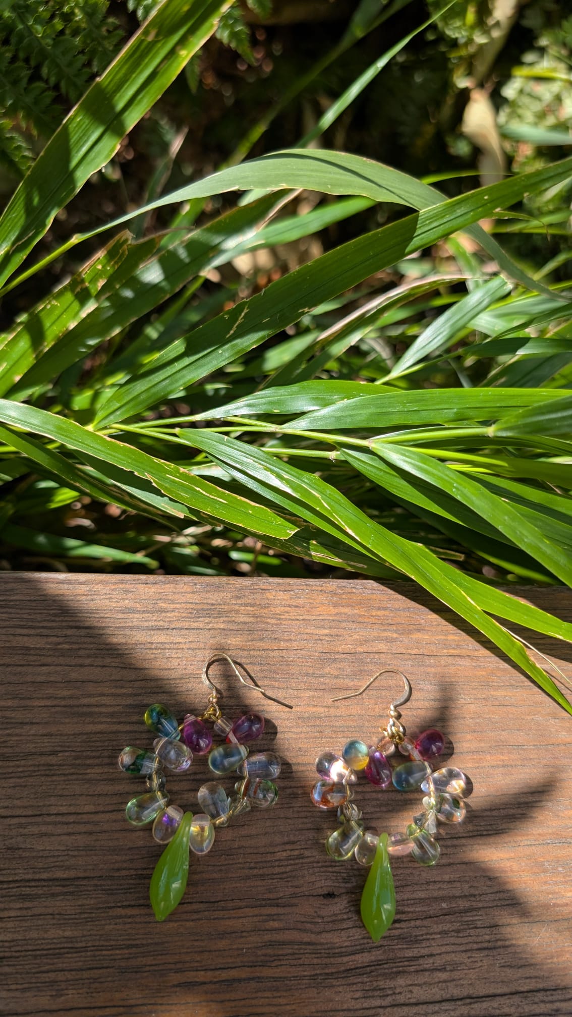 Multicolored round beaded earrings on a wooden surface with green leaves in the background