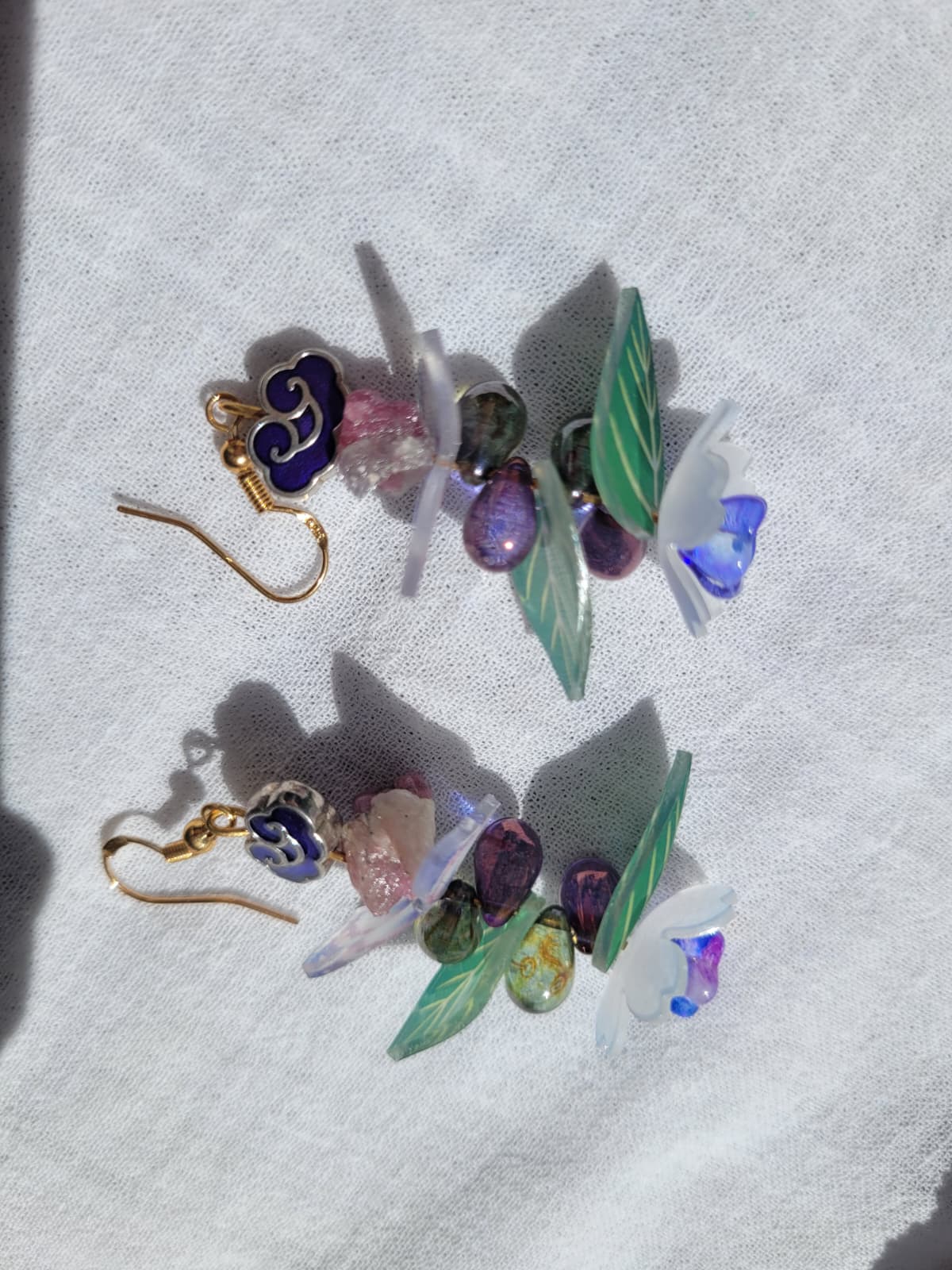 Earrings butterfly, floral and leaves details shaped with Cloisonne cloud-shaped beads on a light background