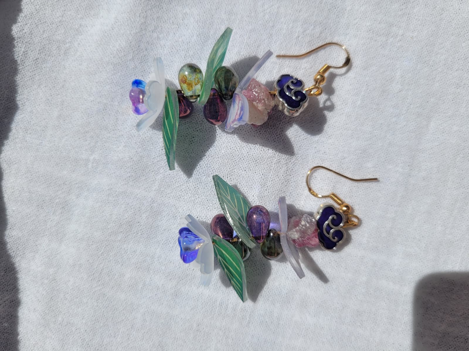 Earrings butterfly, floral and leaves details shaped with Cloisonne cloud-shaped beads on a light background