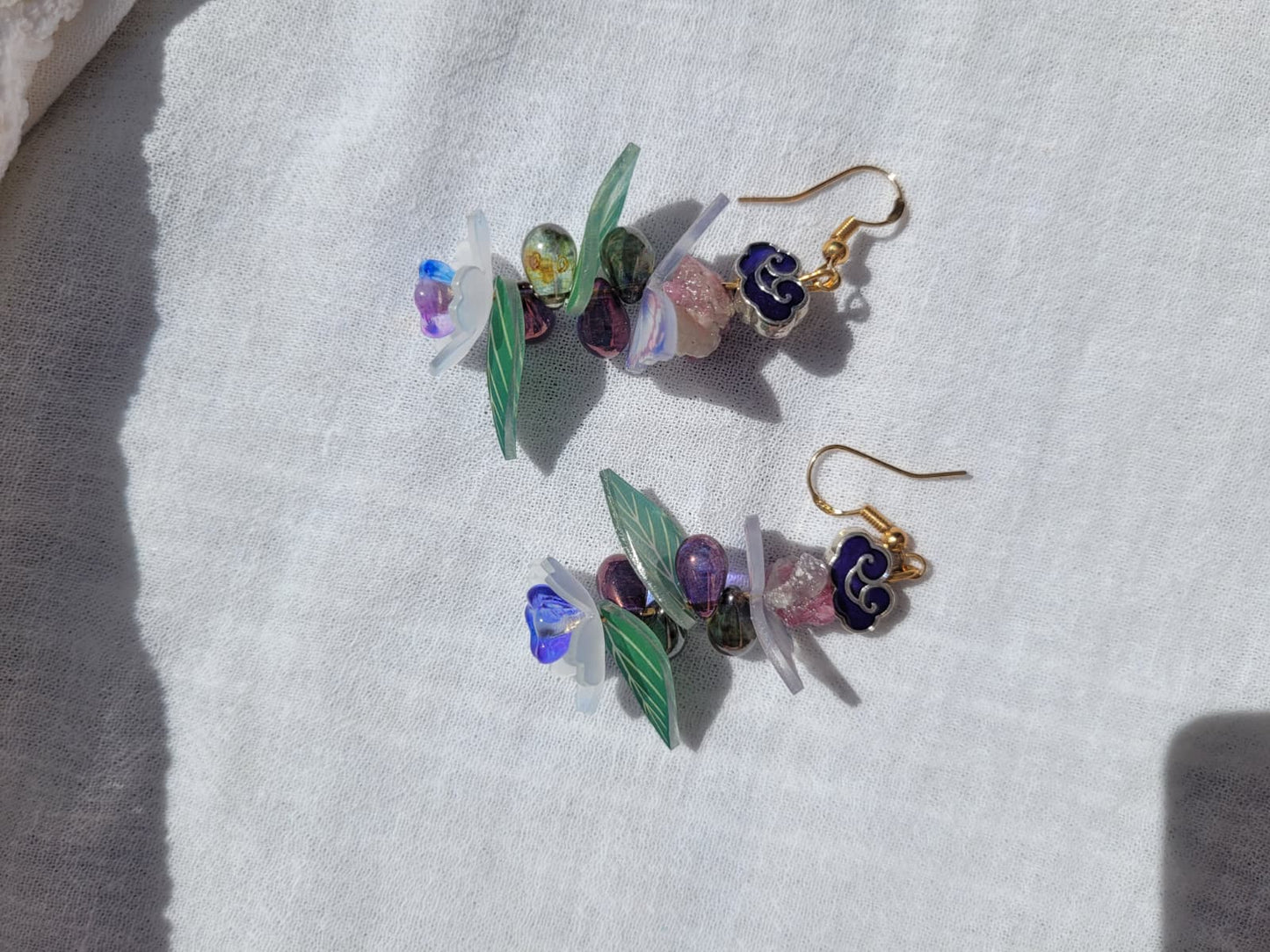 Earrings butterfly, floral and leaves details shaped with Cloisonne cloud-shaped beads on a light background