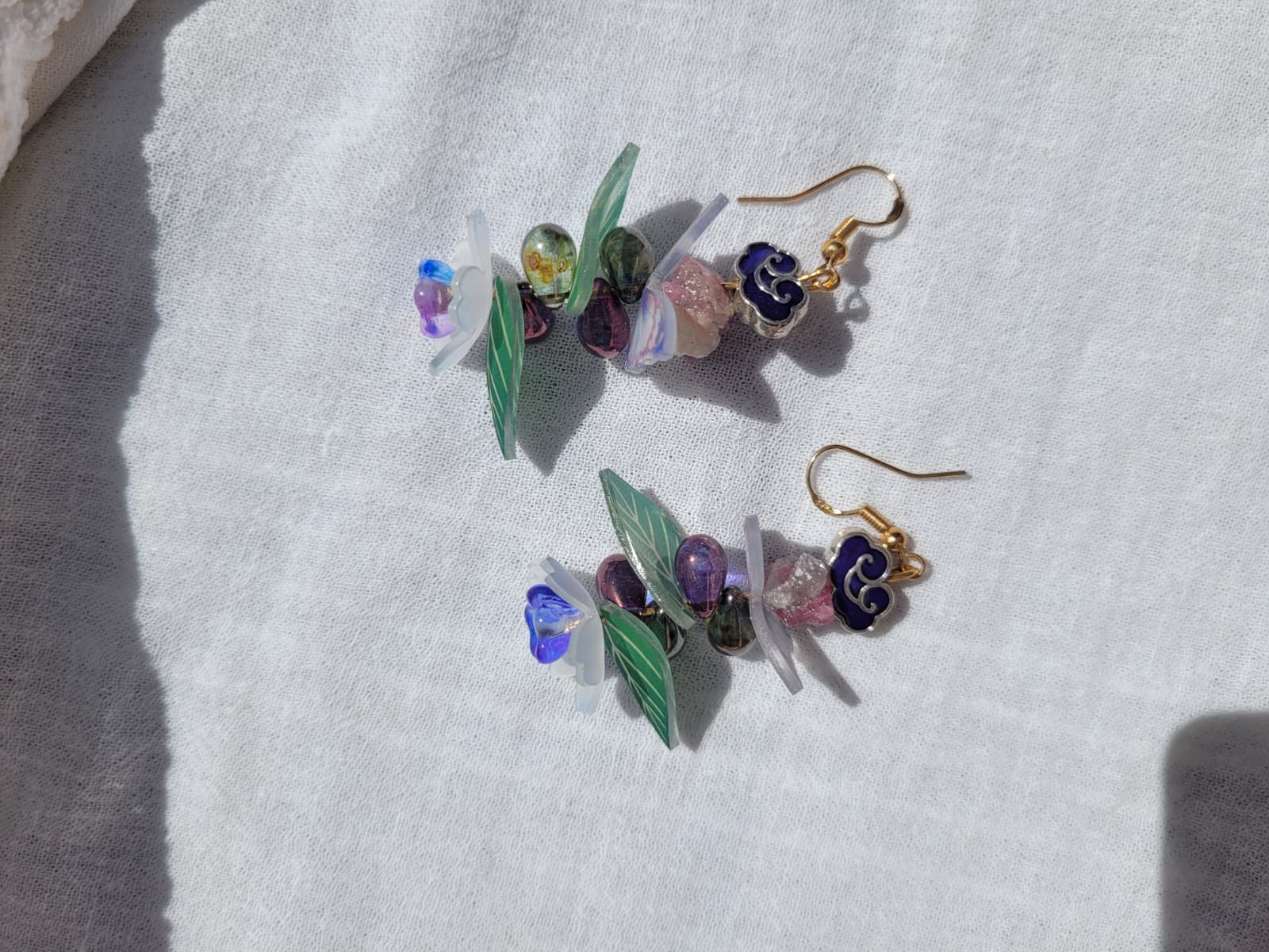 Earrings butterfly, floral and leaves details shaped with Cloisonne cloud-shaped beads on a light background