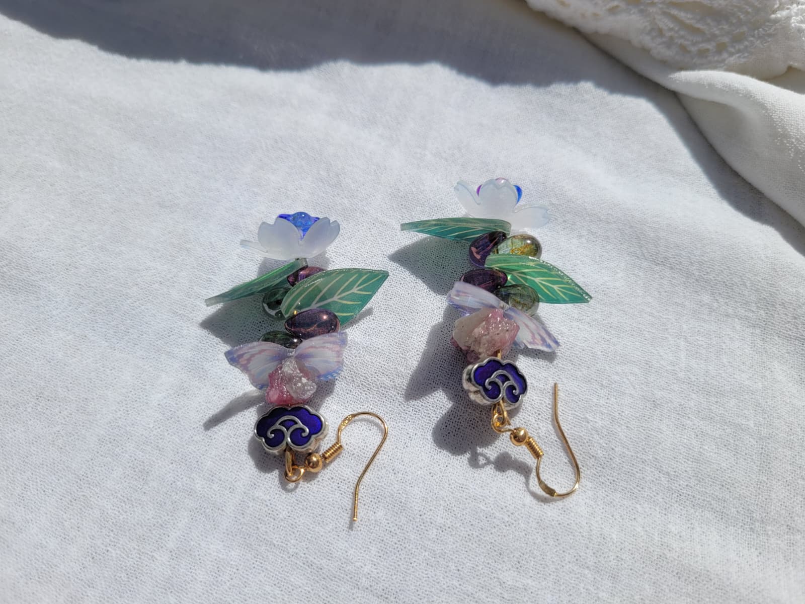 Earrings butterfly, floral and leaves details shaped with Cloisonne cloud-shaped beads on a light background