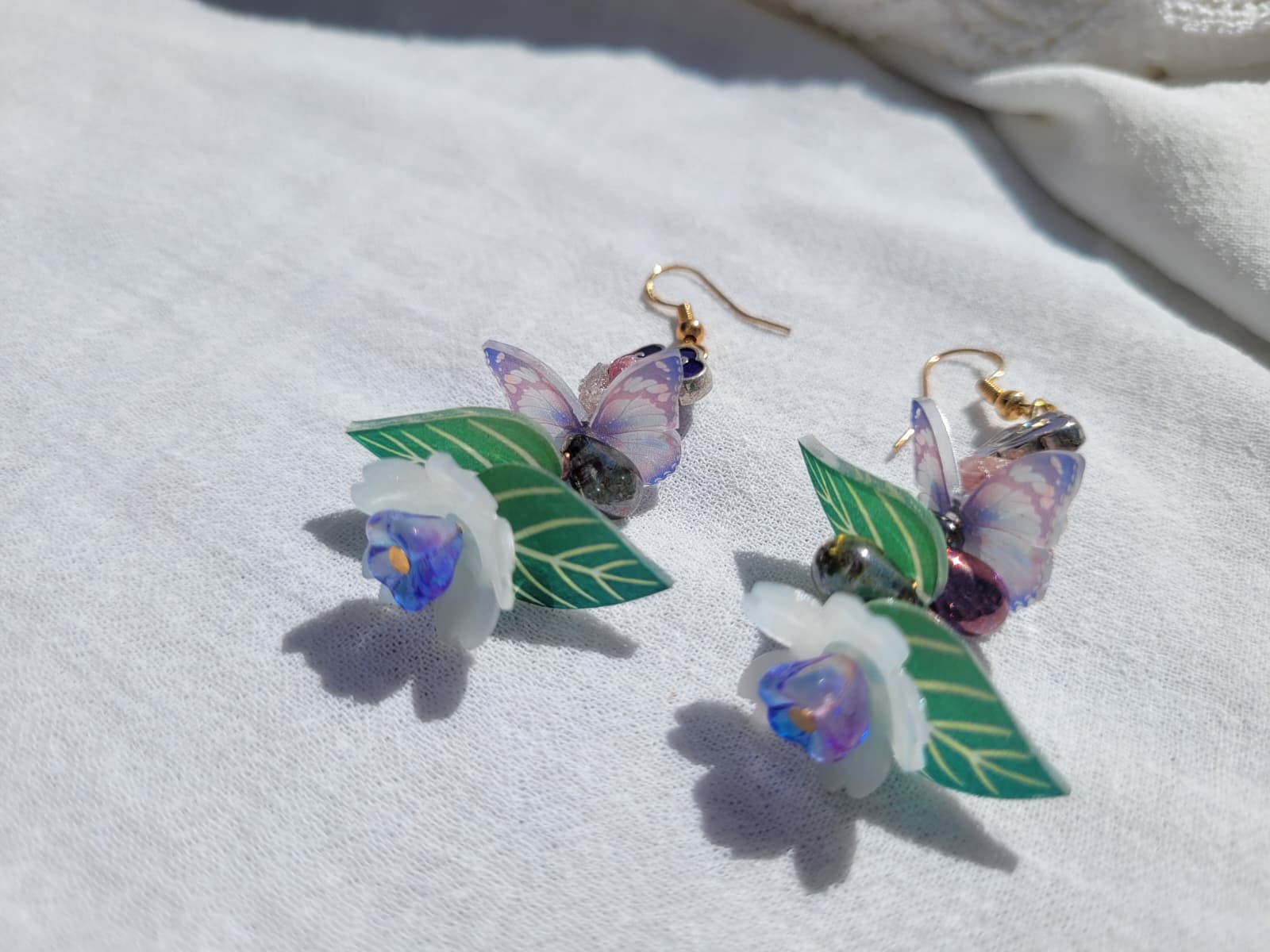 Earrings butterfly, floral and leaves details shaped with Cloisonne cloud-shaped beads on a light background