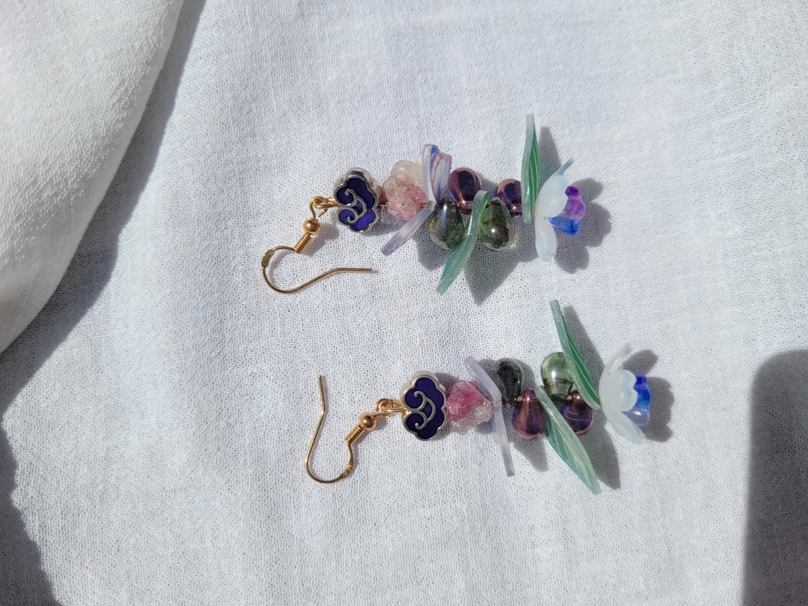 Earrings butterfly, floral and leaves details shaped with Cloisonne cloud-shaped beads on a light background