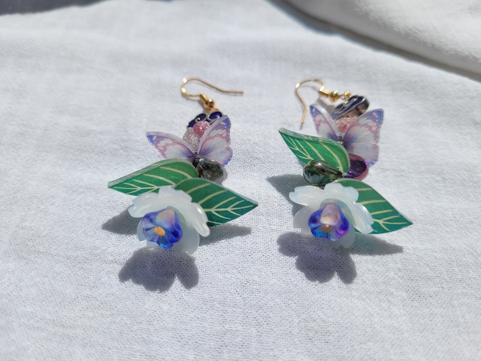 Earrings butterfly, floral and leaves details shaped with Cloisonne cloud-shaped beads on a light background