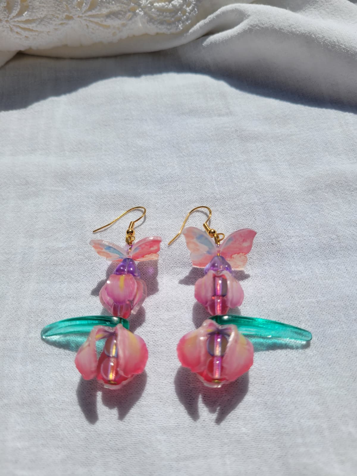 Pink iris-shaped earrings with green leaves and pink butterflies on a light gray fabric background