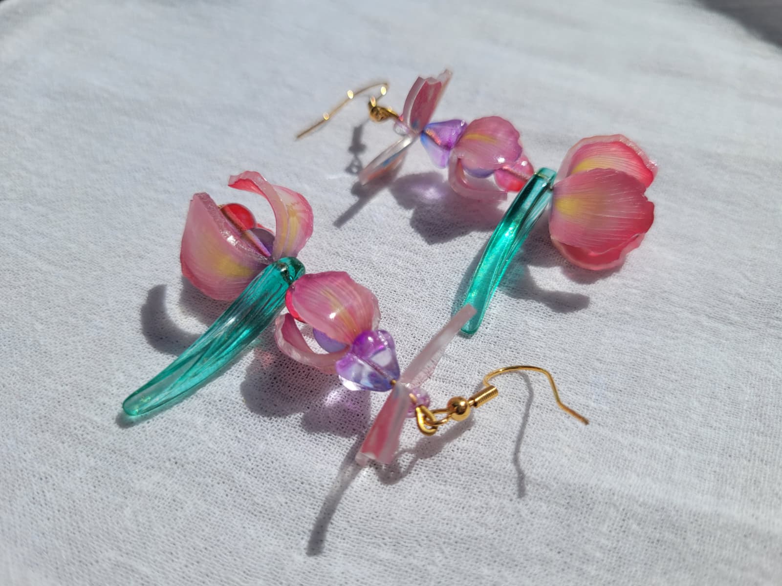 Pink iris-shaped earrings with green leaves and pink butterflies on a light gray fabric background