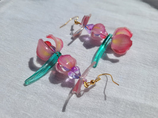 Pink iris-shaped earrings with green leaves and pink butterflies on a light gray fabric background