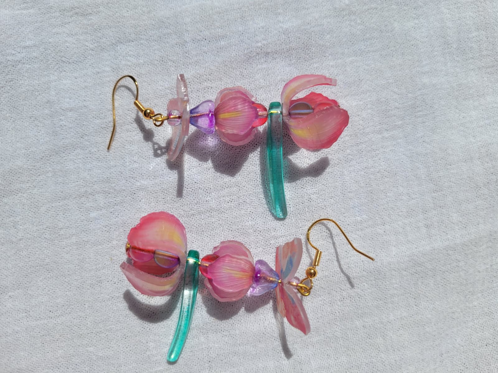 Pink iris-shaped earrings with green leaves and pink butterflies on a light gray fabric background