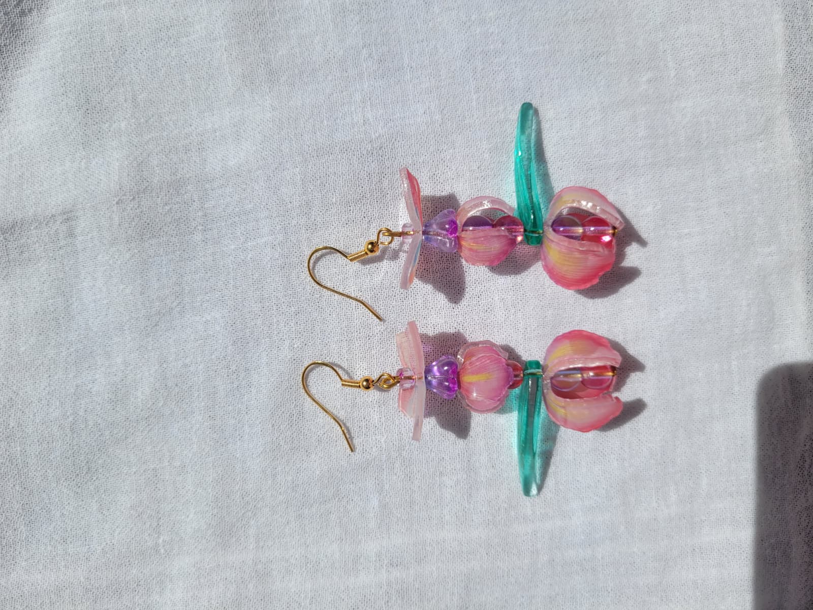 Pink iris-shaped earrings with green leaves and pink butterflies on a light gray fabric background