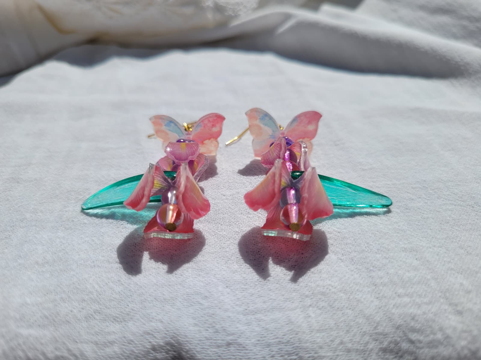Pink iris-shaped earrings with green leaves and pink butterflies on a light gray fabric background
