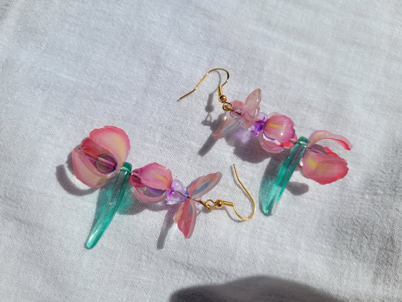 Pink iris-shaped earrings with green leaves and pink butterflies on a light gray fabric background