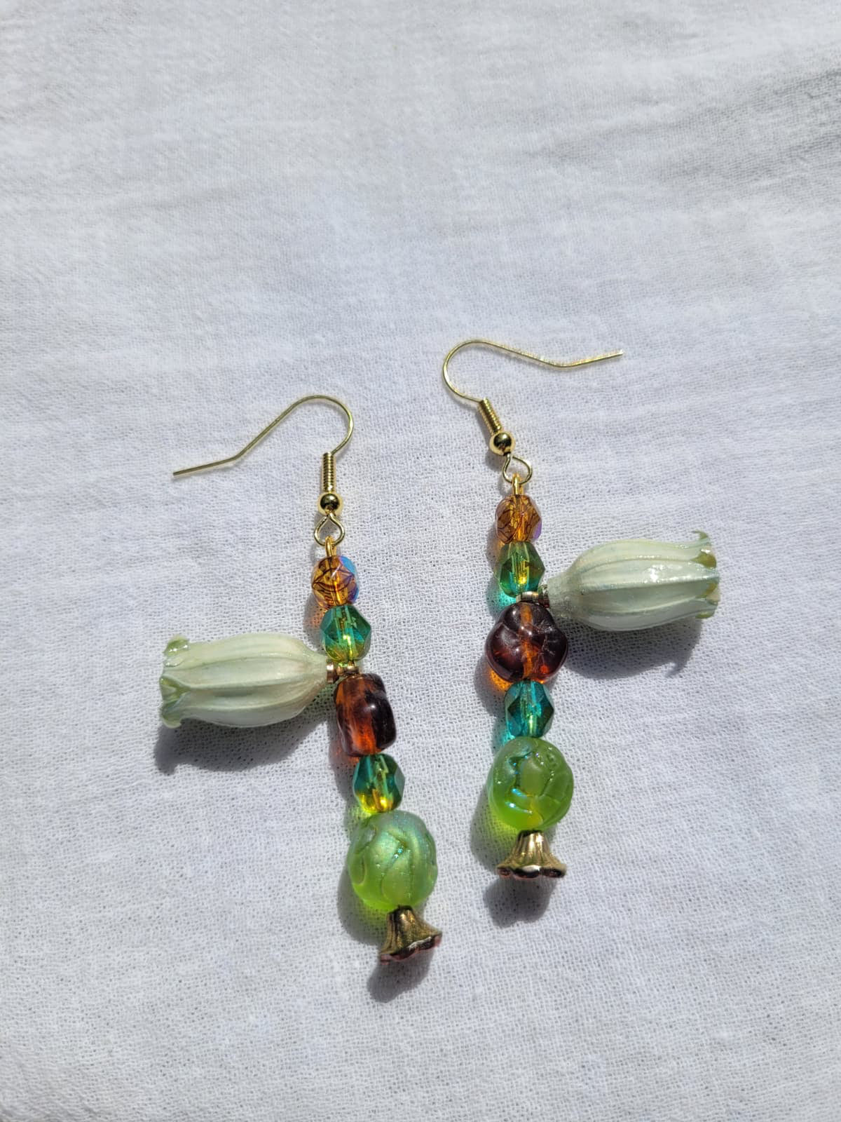 Beaded floral earrings with green and brown beads and natural dried flowers on a light fabric background; gold-coloured hooks.