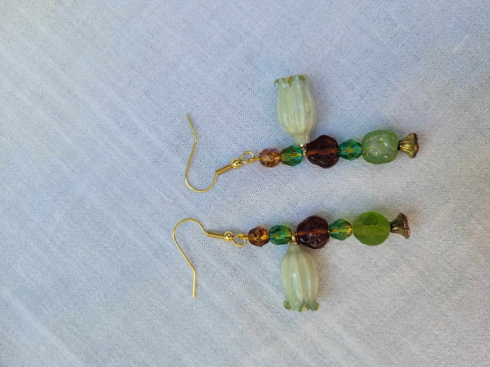 Beaded floral earrings with green and brown beads and natural dried flowers on a light fabric background; gold-coloured hooks.