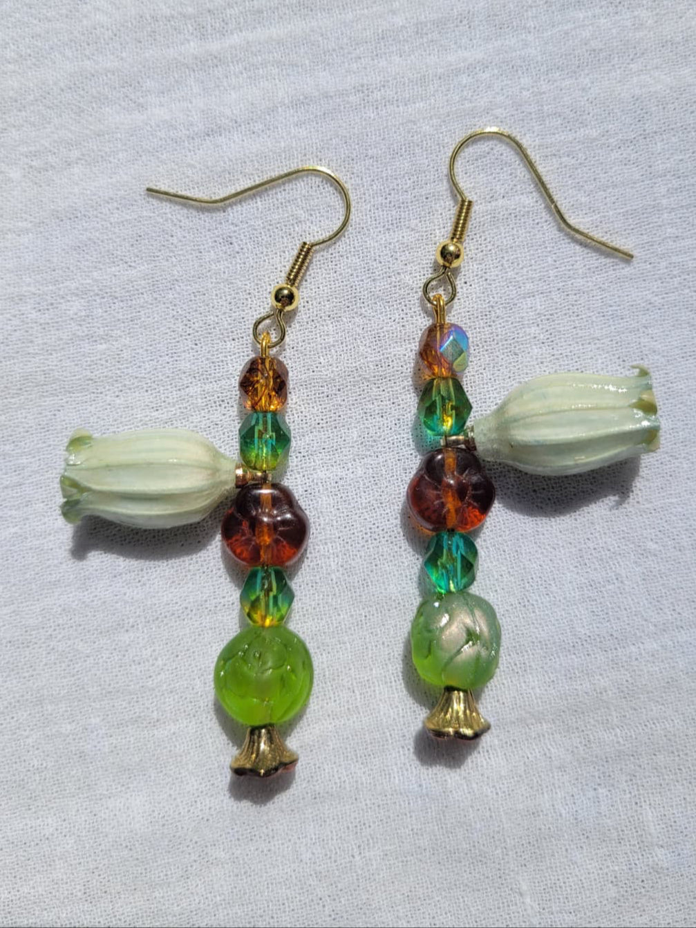 Beaded earrings with green and brown beads and natural dried flowers on a light fabric background; gold-coloured hooks.