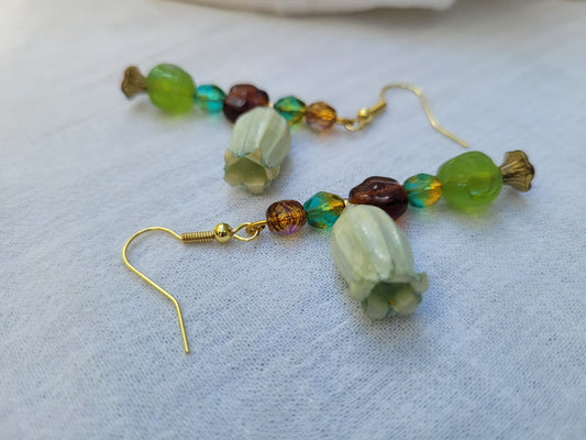 Beaded earrings with green and brown beads and natural dried flower on a light fabric background; gold-coloured hooks.