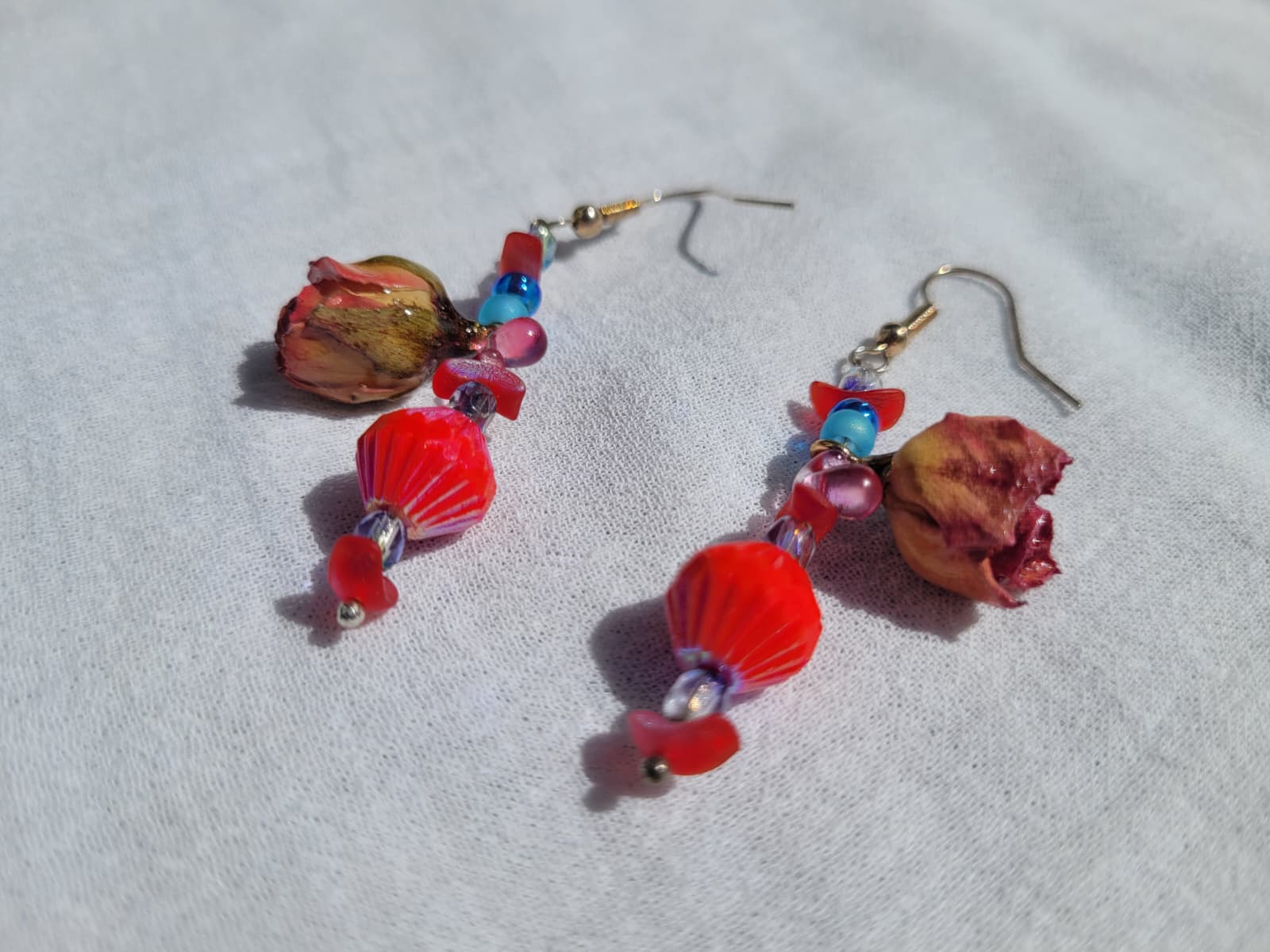 Pair of colorful floral beaded earrings with natural dried blush pink roses and small beads  on a light gray fabric background