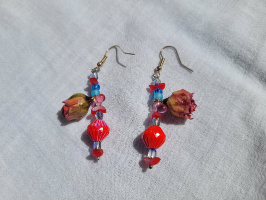 Pair of colorful floral beaded earrings with natural dried blush pink roses and small beads  on a light gray fabric background