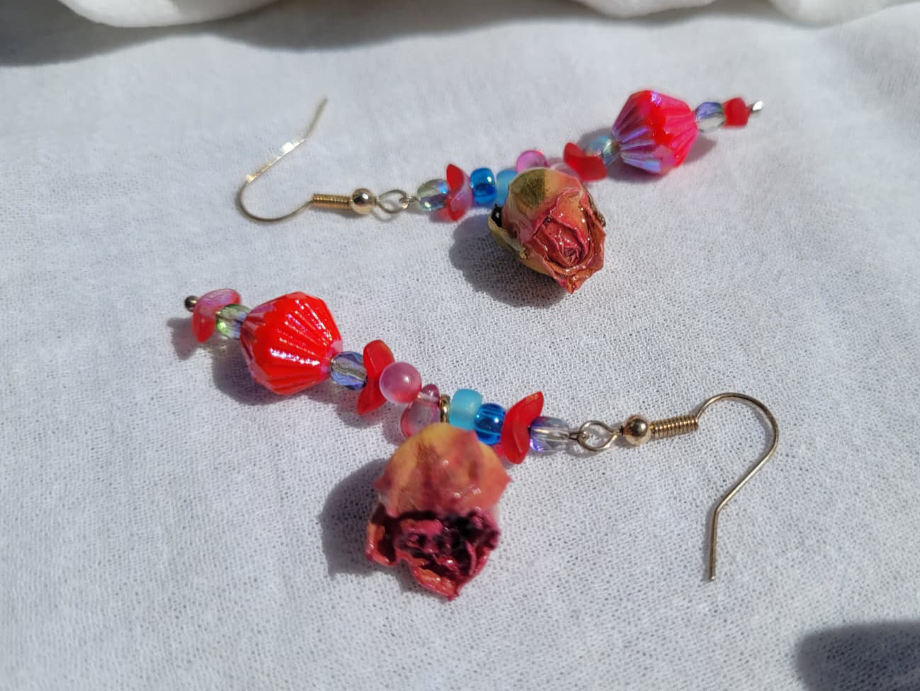 Pair of colorful floral beaded earrings with natural dried blush pink roses and small beads  on a light gray fabric background