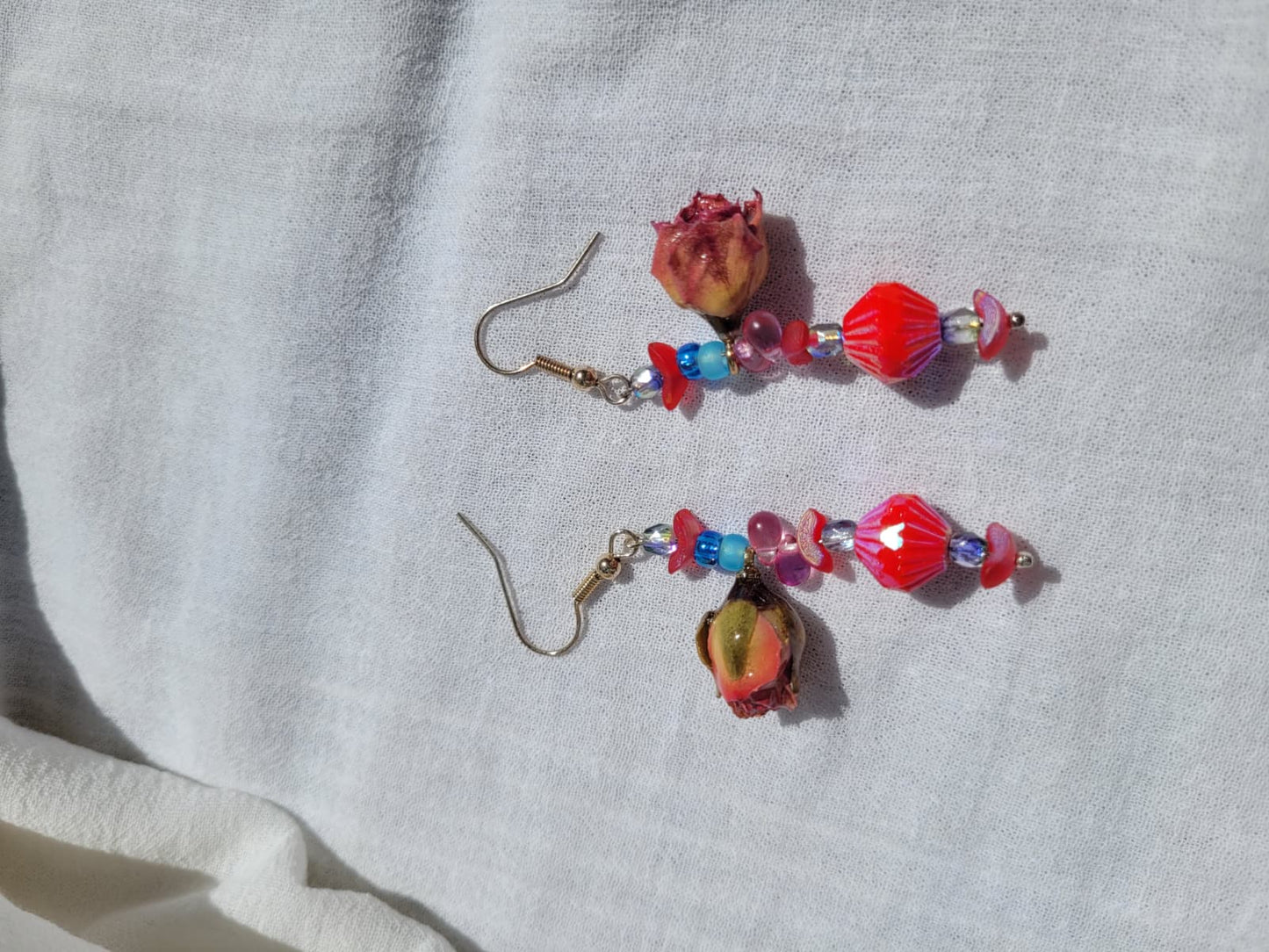 Pair of colorful floral beaded earrings with natural dried blush pink roses and small beads  on a light gray fabric background