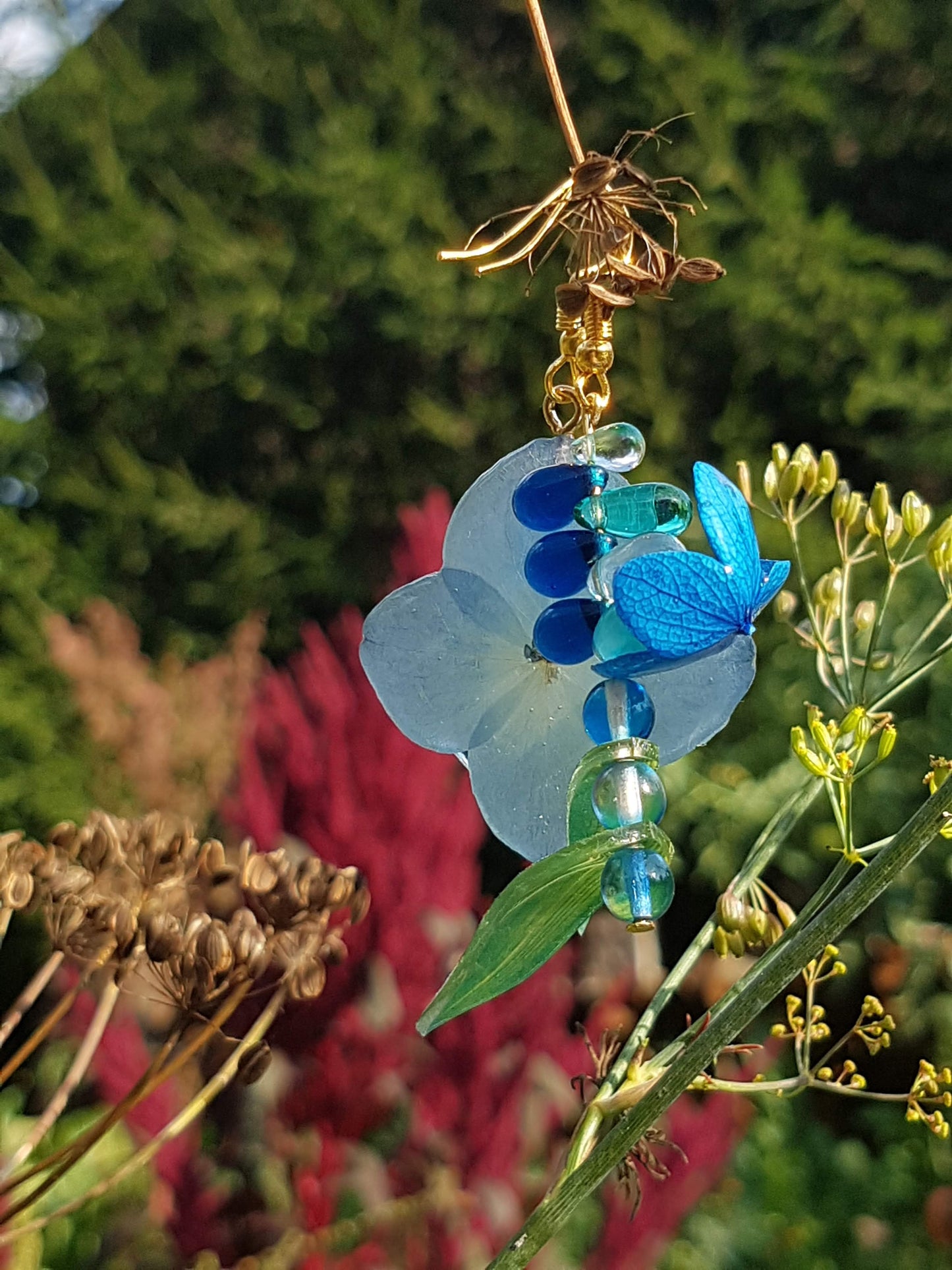 Hydrangea and blue beads earrings on a plant with a blurred natural background
