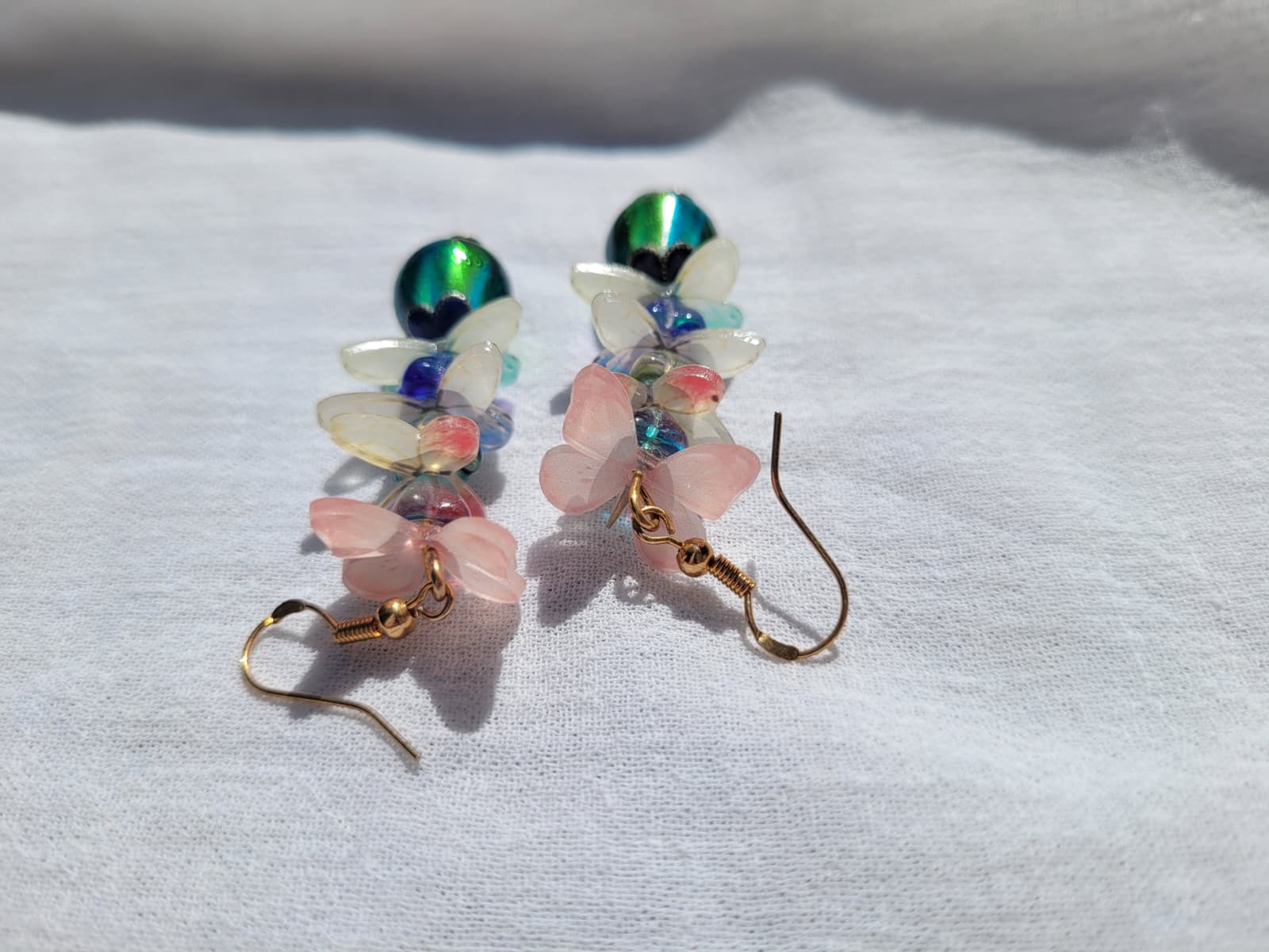 Multicolored butterfly-shaped earrings with gold hooks on a white fabric background